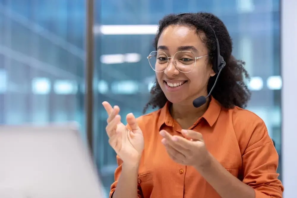 Customer service representative wearing headset smiling while working on laptop in office